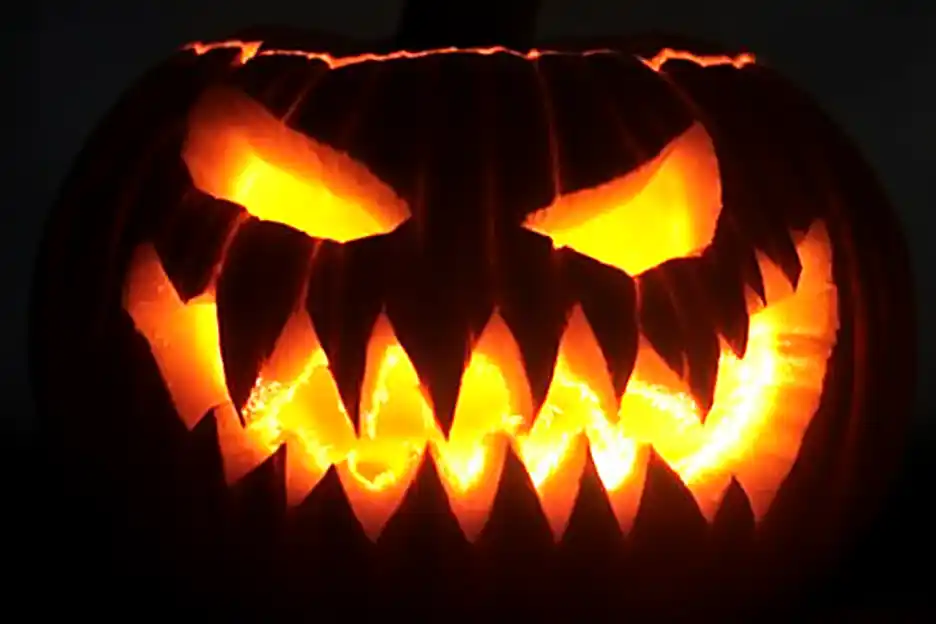 Carved pumpkin with a sinister face, featuring sharp teeth and glowing eyes.