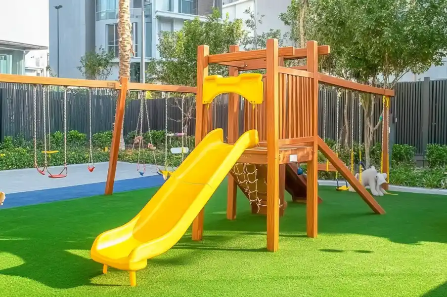 Colorful playground structure with a yellow slide, swings, and climbing elements on a green artificial turf