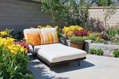 Cozy outdoor lounge chair with orange cushions surrounded by potted flowers and lush greenery in a serene garden setting