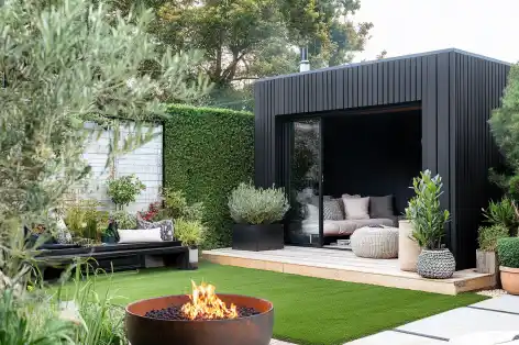 Modern garden with a black shed, potted plants, a fire pit, and cozy outdoor seating