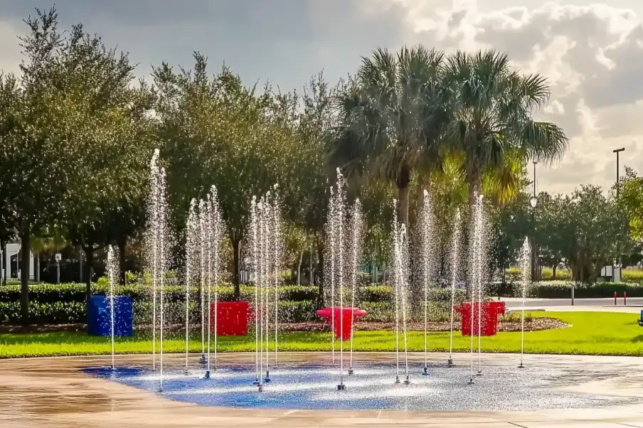 Playful water fountain with arcing streams set against a lush park backdrop, featuring colorful frames and tall palm trees