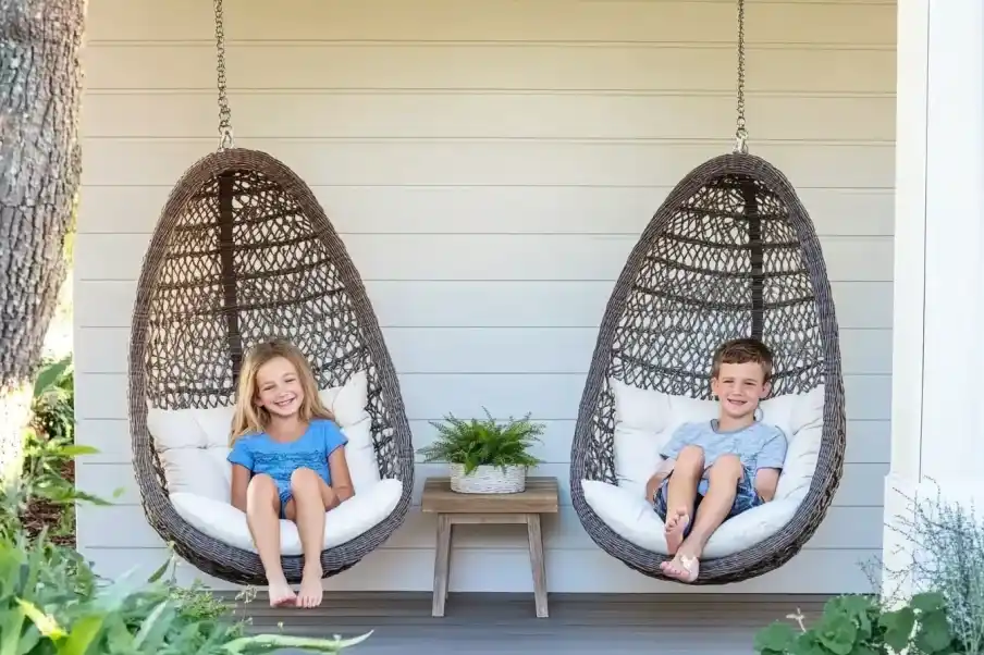 Two children relaxing in cozy hanging chairs on a porch, surrounded by lush greenery