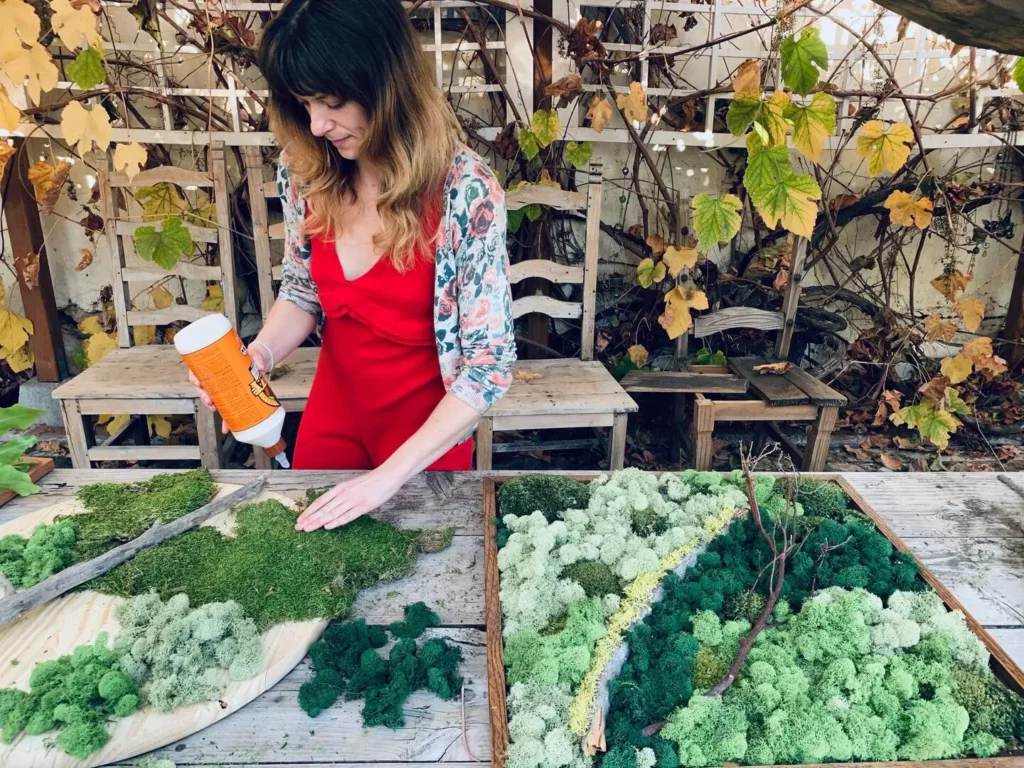 Woman-crafting-a-natural-moss-art-piece-on-a-wooden-table-surrounded-by-autumn-leaves