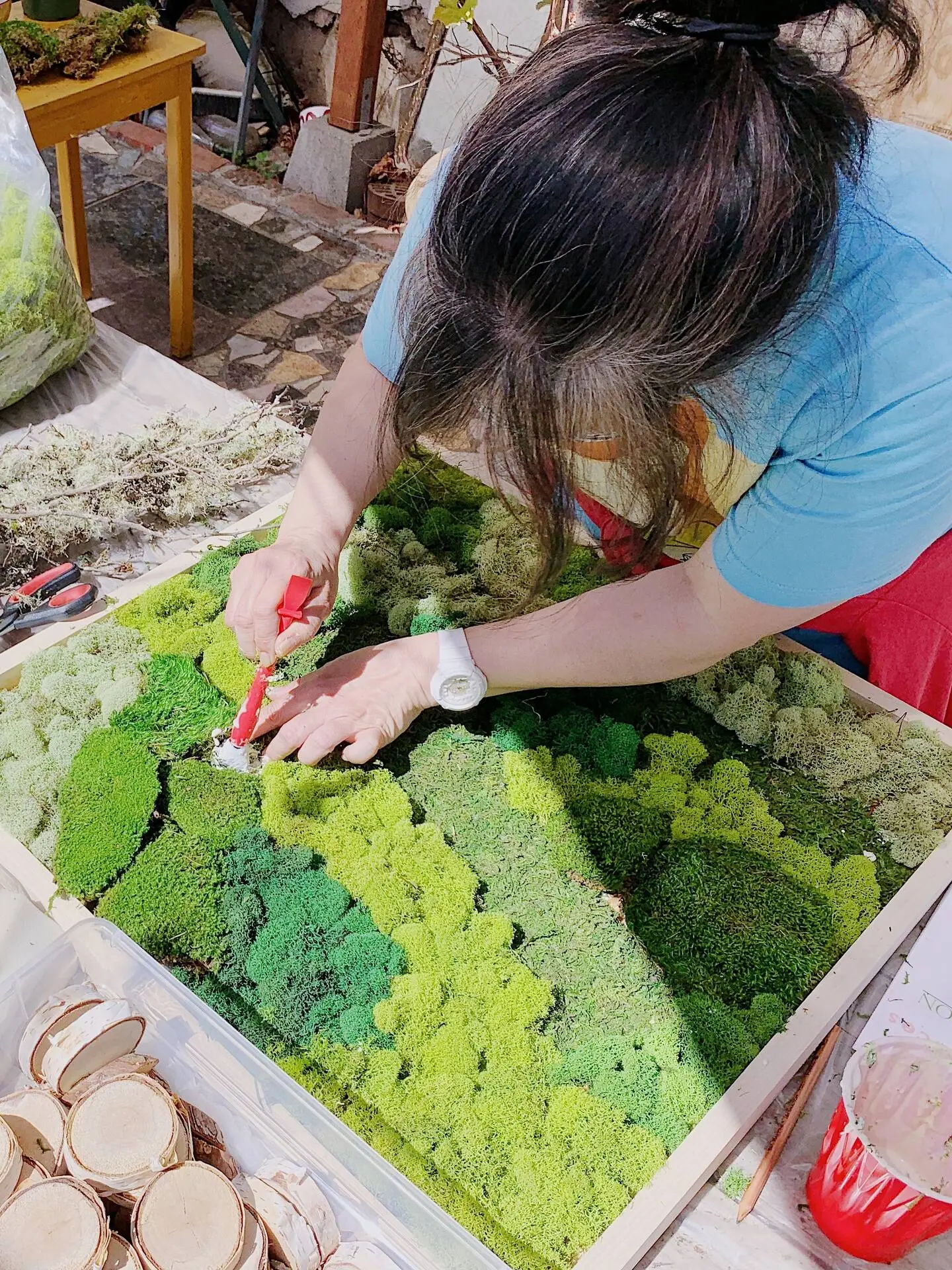 Woman-meticulously-arranging-green-moss-onto-a-wooden-frame-for-a-nature-inspired-artwork