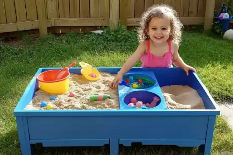 Young girl enjoying a DIY outdoor sensory table with separate water and sand play areas