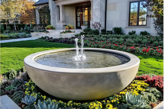 Modern circular water fountain in a landscaped garden in front of a house