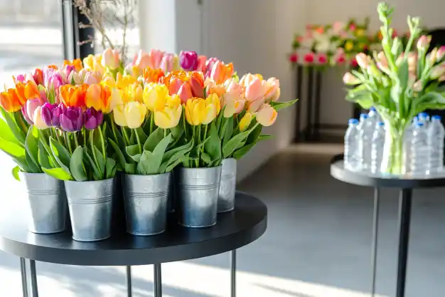 Buckets of colorful tulips, ranging from orange to purple, displayed on sleek black tables in a minimalistic flower shop