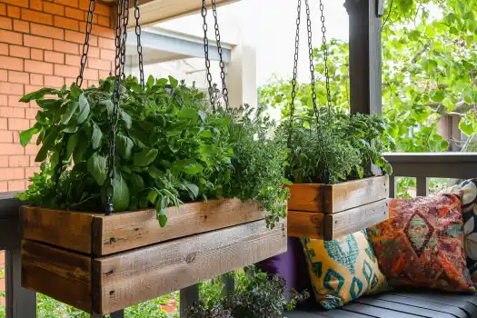 Hanging wooden planters filled with fresh herbs, such as basil and mint, create a cozy and aromatic addition to a porch adorned with colorful pillows.