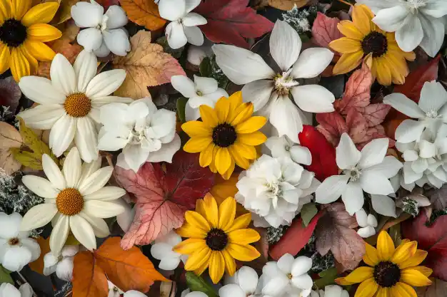 A vibrant autumnal arrangement featuring a mix of bright yellow, white flowers, and colorful fall leaves in shades of red, orange, and brown, creating a festive seasonal display