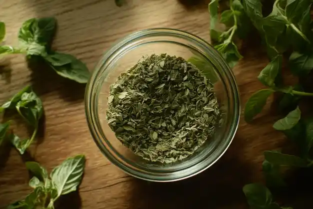 A jar filled with dried oregano leaves, surrounded by fresh green oregano sprigs on a wooden surface, bathed in warm light.