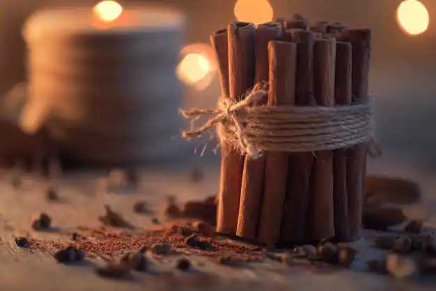 A neatly bundled stack of cinnamon sticks tied with twine, surrounded by loose cinnamon powder and cloves, illuminated by soft, cozy lighting.