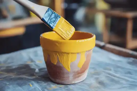 A close-up of a terracotta pot being painted with bright yellow paint, showcasing the initial stages of a creative DIY garden project.