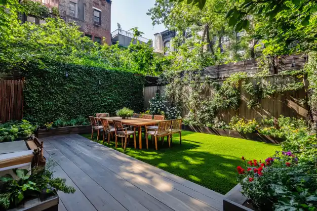 A vibrant backyard garden with a wooden dining table set surrounded by ivy-covered walls and blooming flowers.