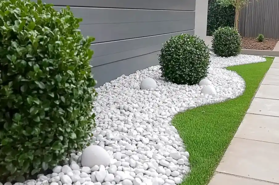 Minimalist front yard design featuring neatly trimmed green shrubs, white decorative pebbles, and a vibrant green lawn bordered by a clean, modern pathway