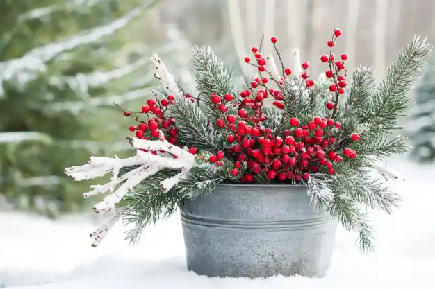 Two ornate planters filled with winter greenery and adorned with warm glowing fairy lights, creating a cozy ambiance in a snow-covered garden at twilight.