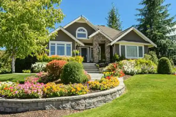 A suburban house with a colorful flower garden and lush green lawn.