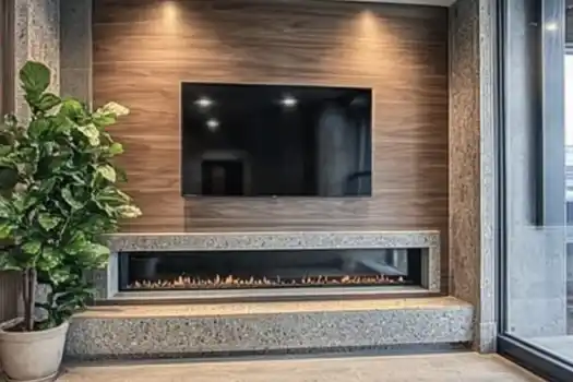 A modern living room with a wall-mounted TV above a sleek, linear fireplace, complemented by a potted plant on the side and large glass windows.